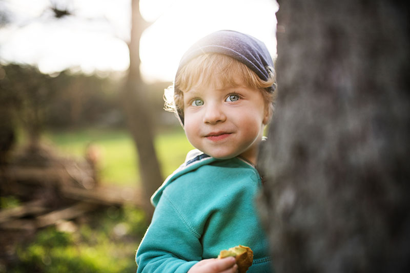 A happy toddler boy hiding behind a tree